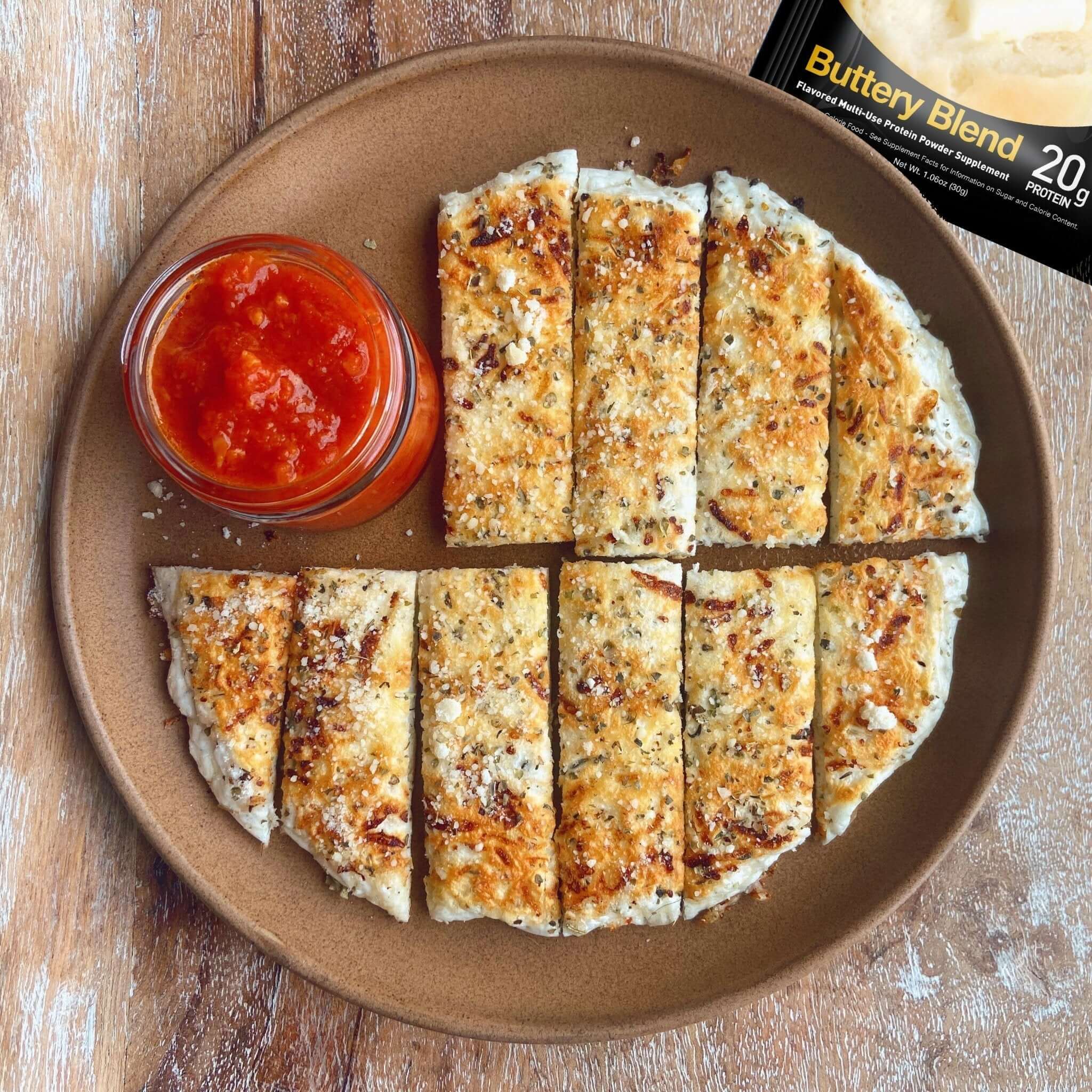 Sliced protein cheese bread on a plate with a side of red sauce, on a wooden surface.