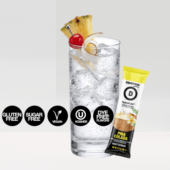 A Devotion Nutrition HydroFlex Pina Colada flavored powder bag stands next to a glass of iced water with pineapple cherry and lime garnish plus a single stick pack. The packaging is white black and yellow with fruit and coconut graphics.