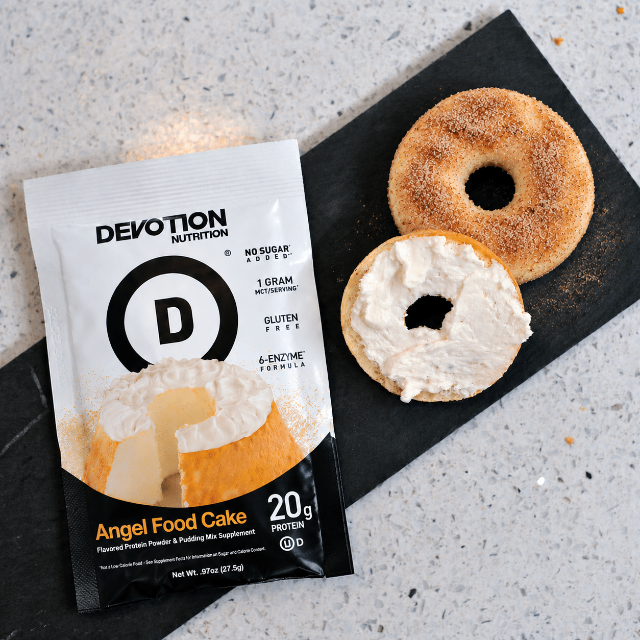 Devotion Nutrition Angel Food Cake protein powder packet with 20g protein, next to a homemade cinnamon sugar protein bagel