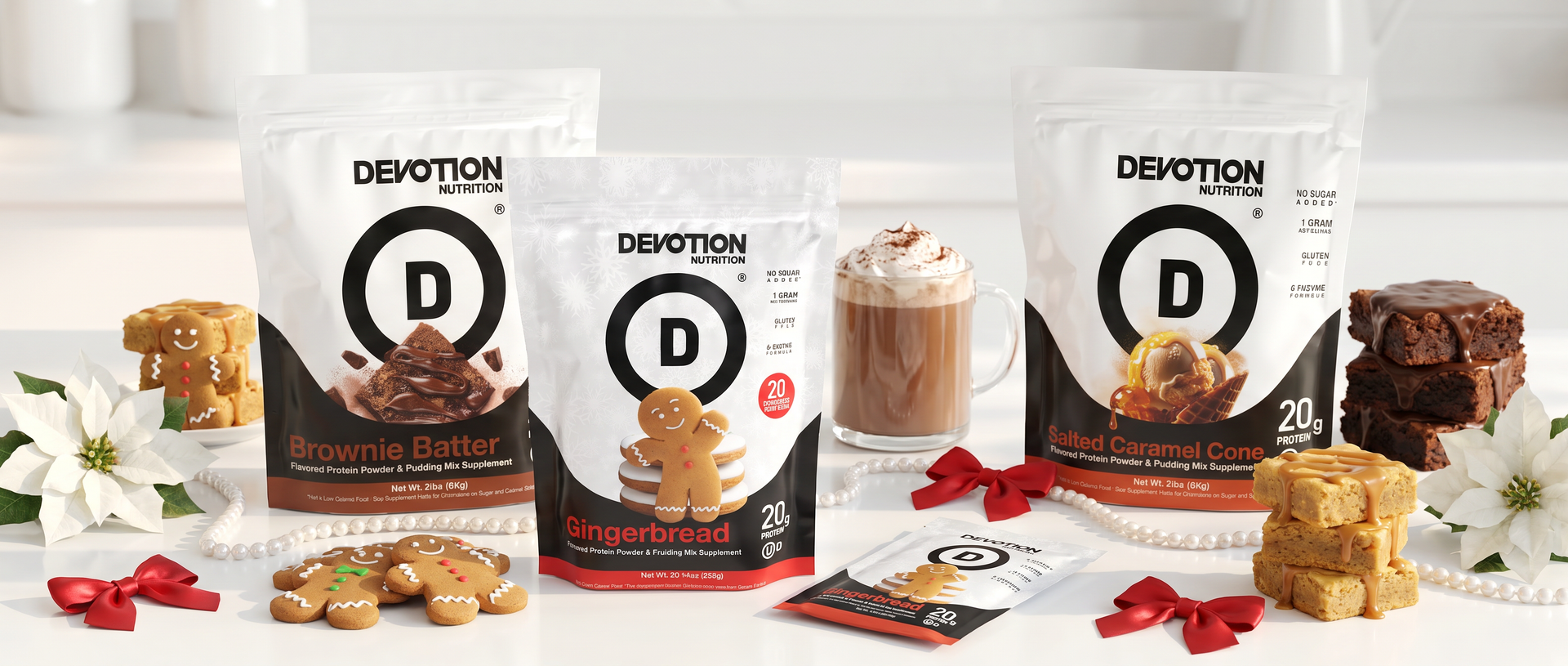 Three Devotion Bakery snack pouches arranged on a white surface with cookies, a mug of hot chocolate, and white flowers. The pouches are labeled Brown Butter, Gingerbread, and Caramel Apple, with a single packet in front.