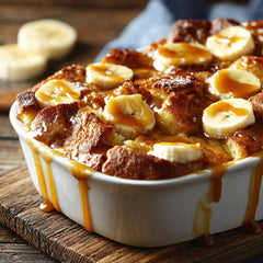 Banana bread pudding with caramel sauce in a white dish on a wooden surface