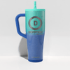 A tall handled tumbler with a teal-to-blue gradient body, a blue handle, and a teal straw lid. The front features a large circular 'D' logo with the word 'DEVOTION' and smaller 'NUTRITION' text below, plus 'ICE shAKER' near the bottom.