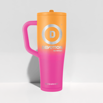 A tall insulated travel mug with a lid and handle  featuring a bright orange-to-pink gradient body. The front has a large silver circular 'D' logo with the word 'DEVOTION NUTRITION' underneath  and 'ICESHAKER' near the bottom.