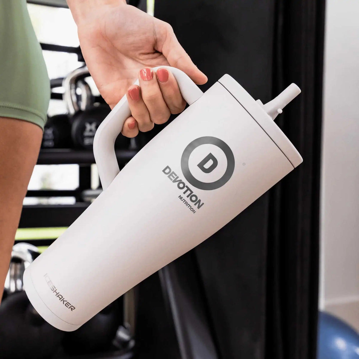 White shaker bottle with 'Devotion' logo held by a person in a kitchen setting.
