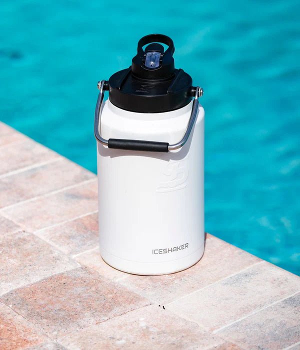 White ice shaker with black lid on a stone surface by a pool