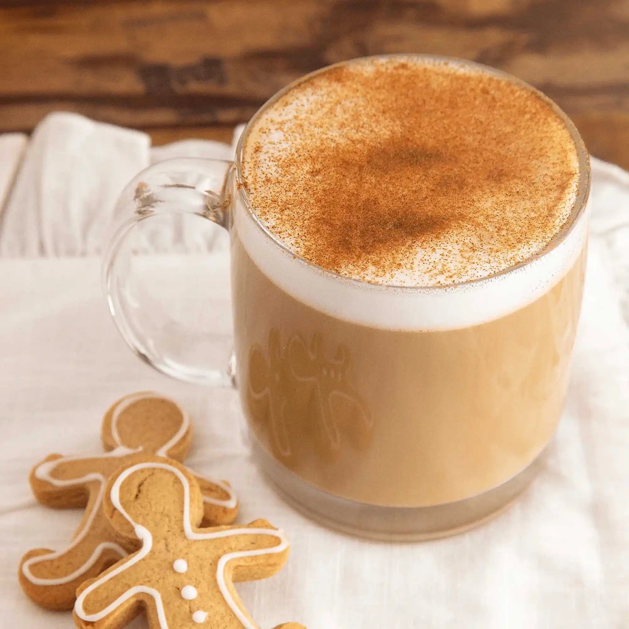 Glass mug of cappuccino with a gingerbread man cookie on a wooden surface