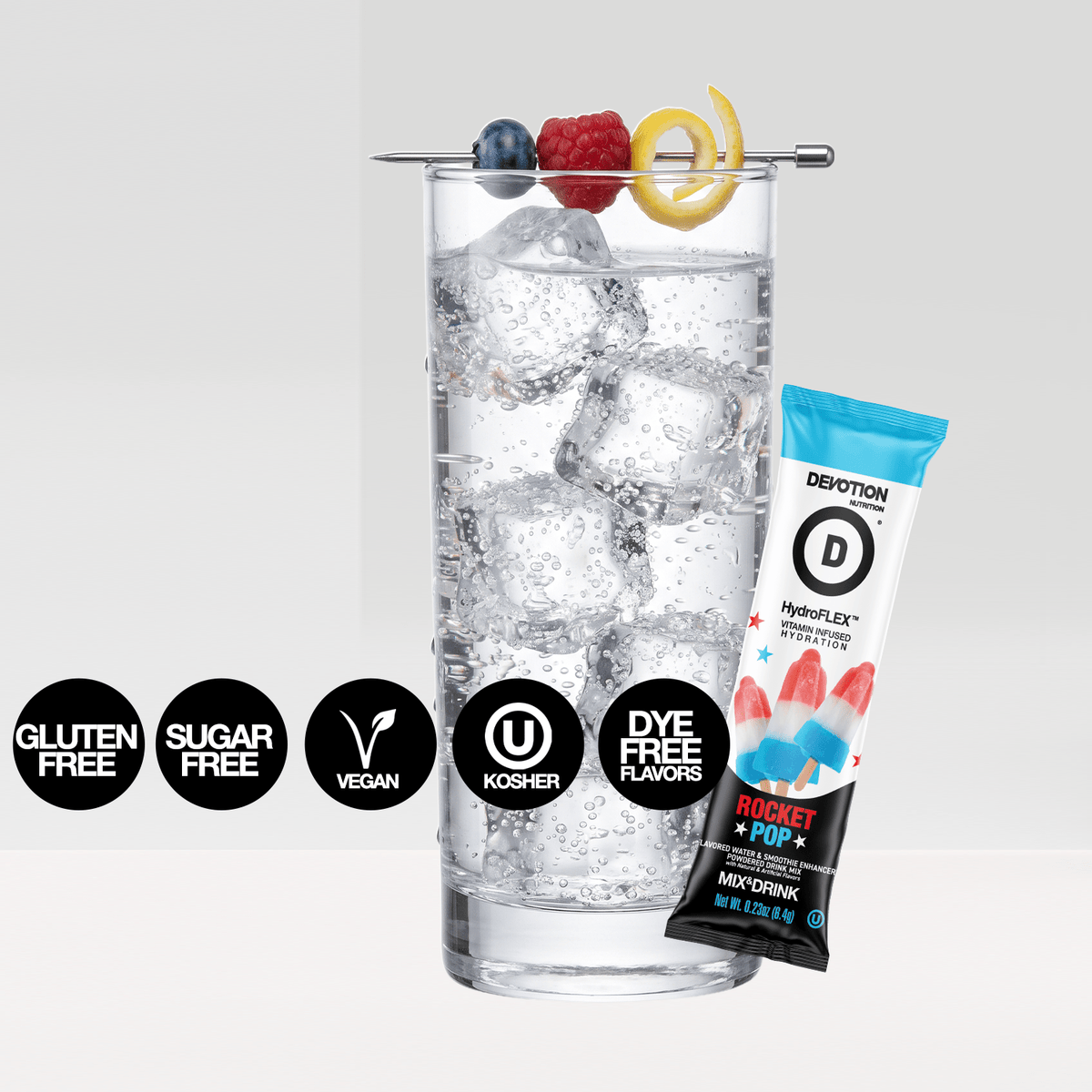 A Devotion HydroFlex protein powder stick pack in Rocket + Pop flavor, shown next to a tall glass of sparkling water with ice and fruit garnishes, with black circular badges indicating gluten free, sugar free, vegan, kosher, and dye free flavors.