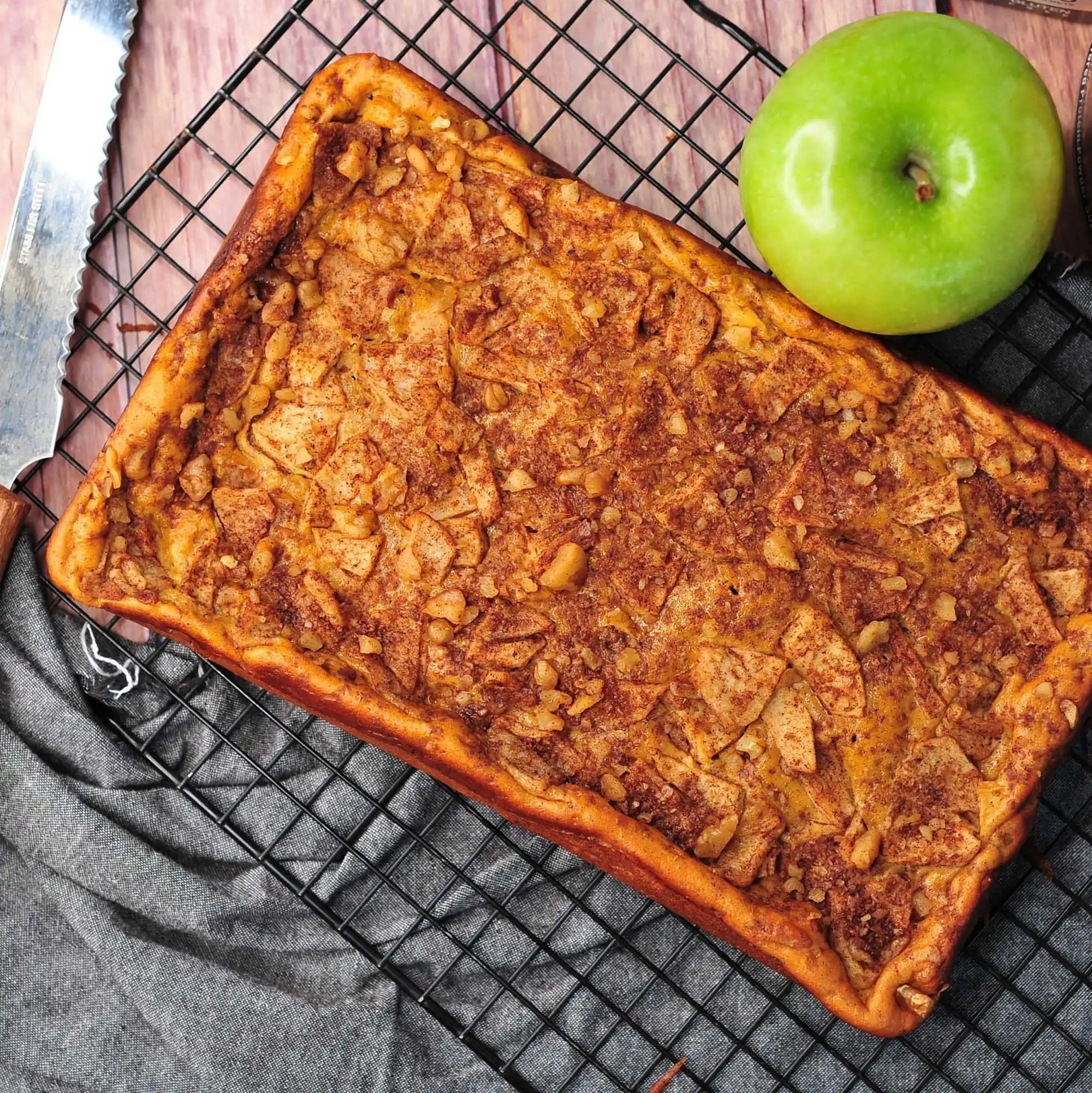 Baked apple slab pie on a cooling rack with a green apple beside it